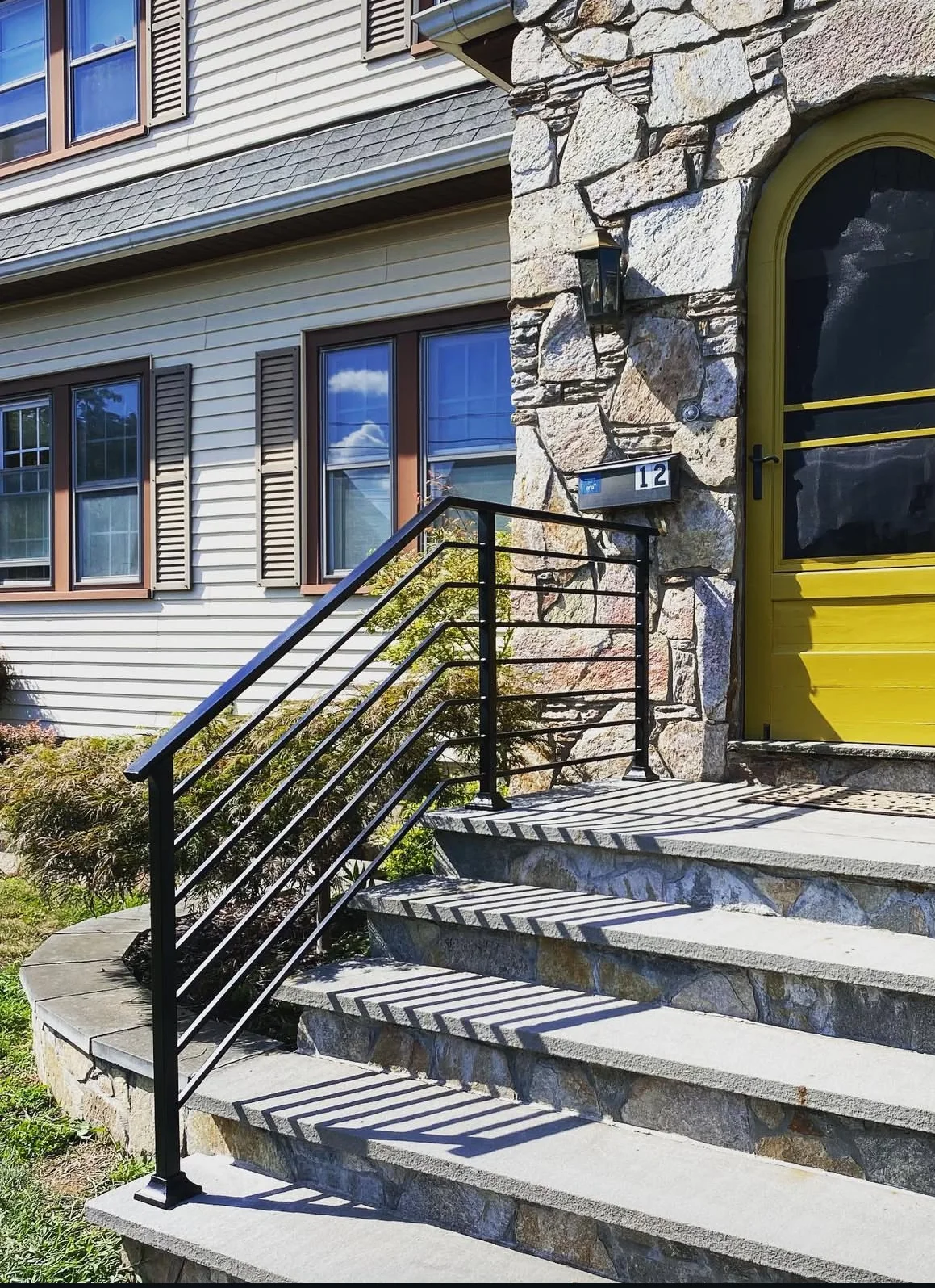 Black horizontal-bar steel railing on granite steps beside a stone entryway with a yellow door