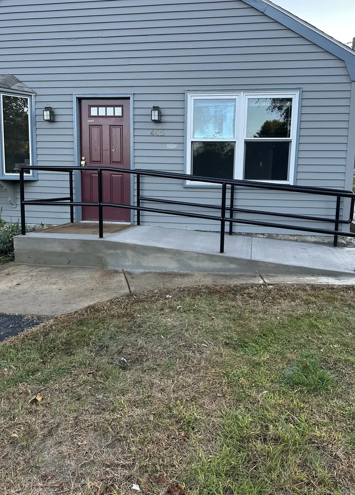 Black steel accessibility ramp railing running along a concrete ramp to a building entrance