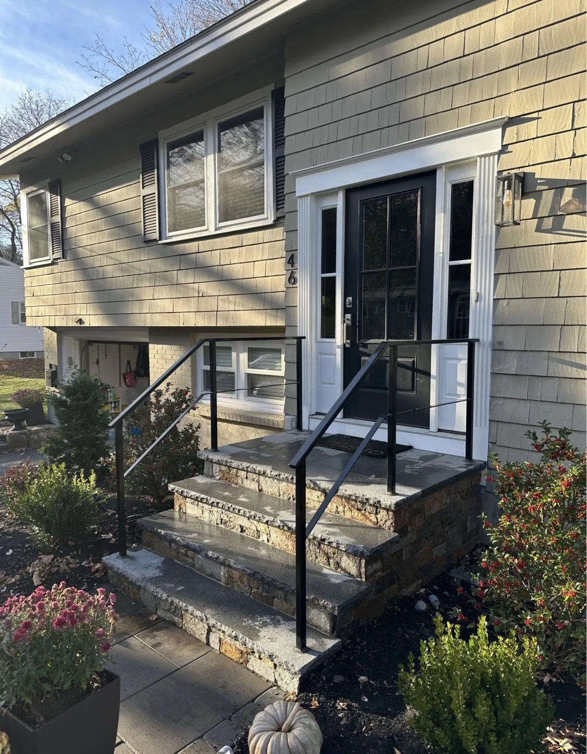 Minimal black steel railing on a granite and fieldstone entry with a black panel front door
