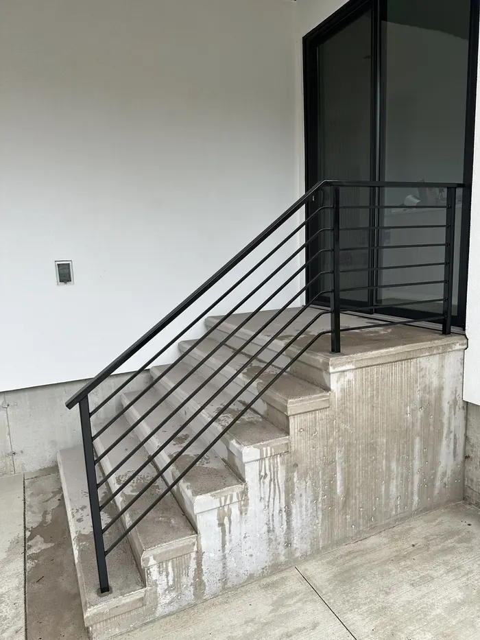 Horizontal-bar black steel railing on cast concrete steps against a white wall